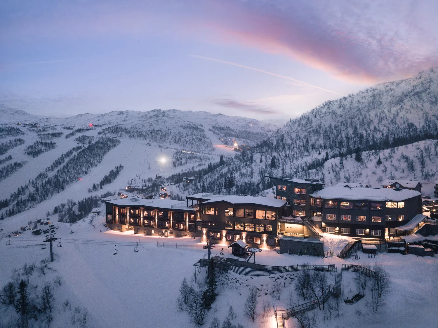 Evening drone shot of a mountain hotel in a winter destination Hotel in snowy mountains in a ski area at dusk with warmly lit rooms