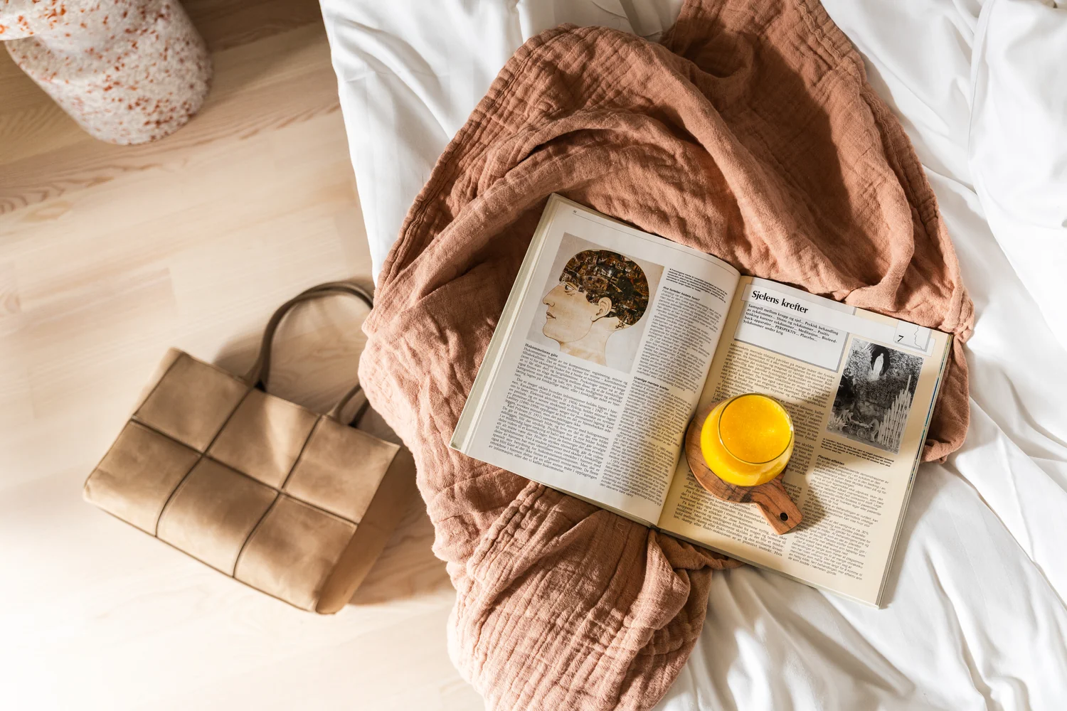 Carefully styled hotel room scene with welcoming details and natural light Stylish hotel room scene with bed, linen blanket, open book and fresh orange juice