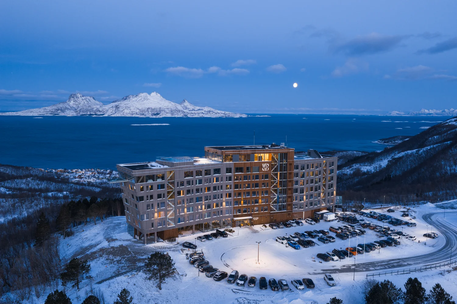 Modern hotel exterior photographed in a dramatic winter setting at dusk Modern hotel in a winter mountain landscape with sea view at dusk
